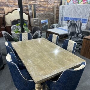 Elegant six-seater dining table set with a marble-look top and navy-blue velvet chairs in a furniture showroom.