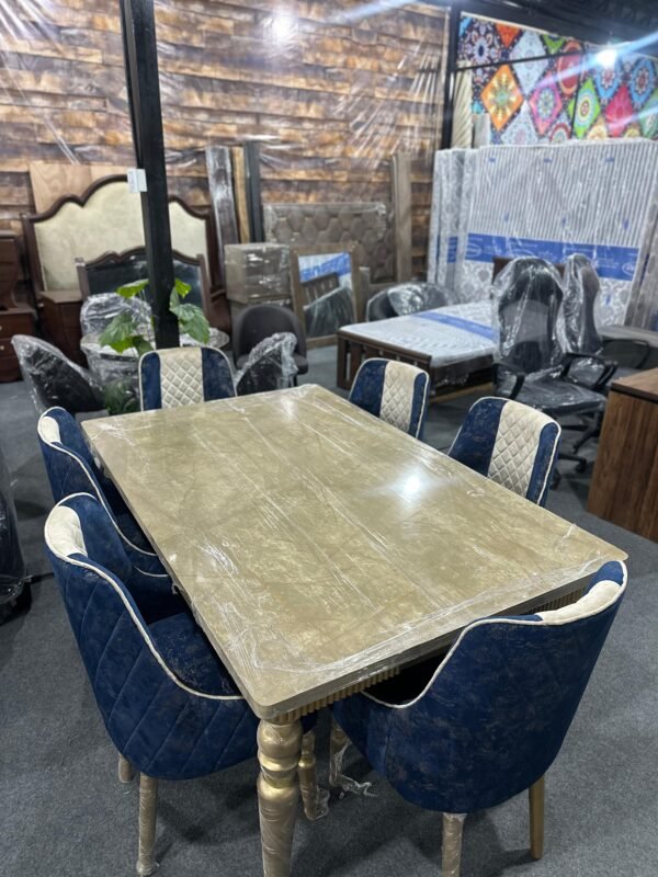 Elegant six-seater dining table set with a marble-look top and navy-blue velvet chairs in a furniture showroom.